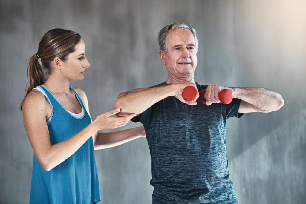 Trainer guiding an older adult with light dumbbells