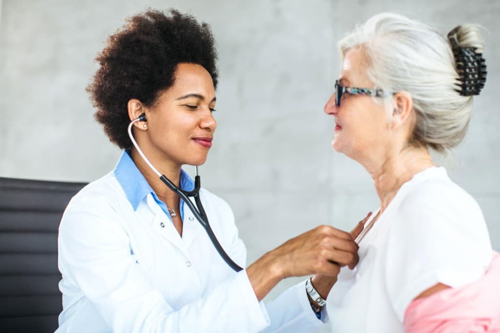 Doctor examining an older adult with a stethoscope in a bright clinic