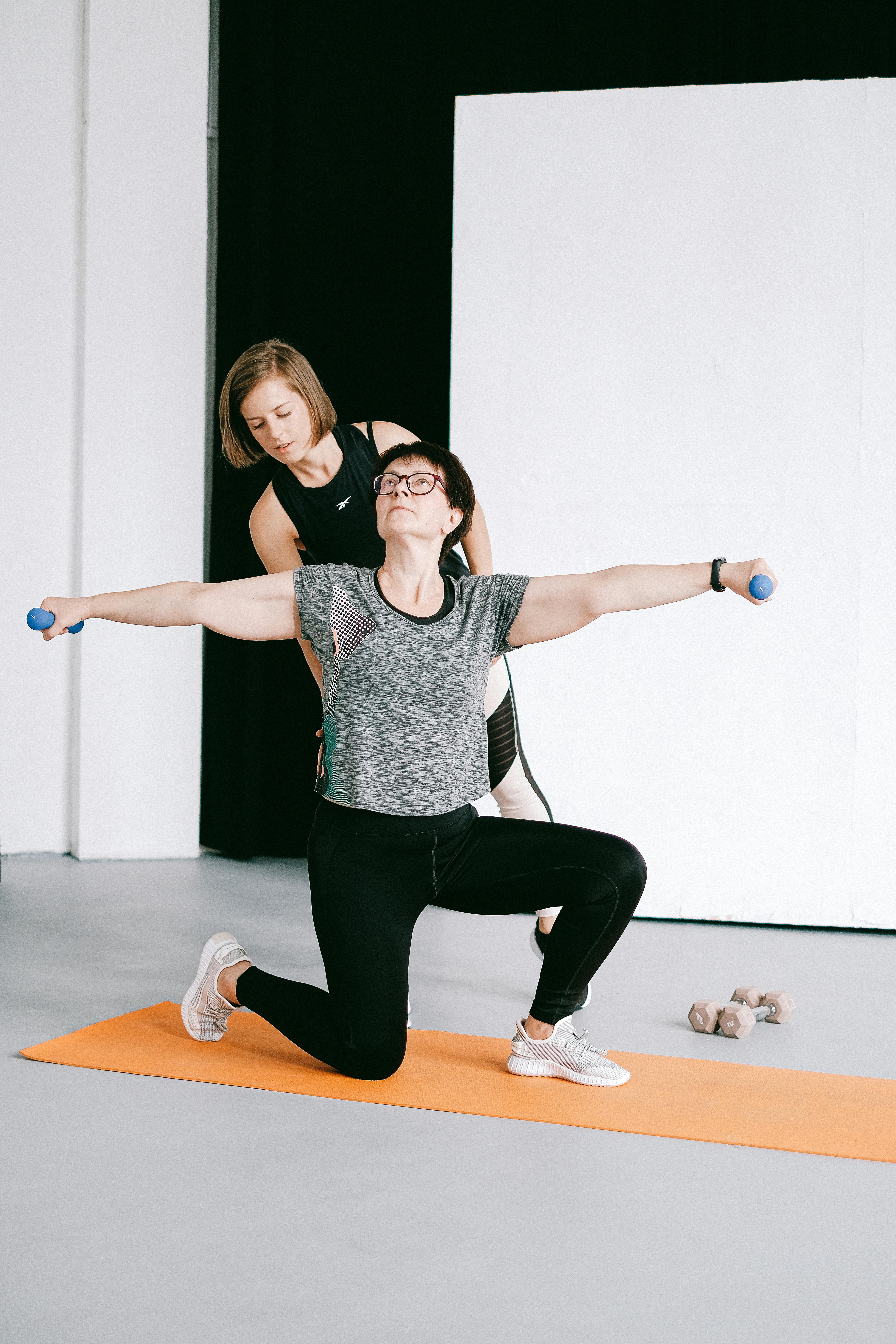 A professional guides an older adult through a gentle strength and balance exercise in a bright studio
